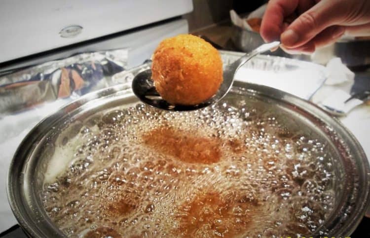 arancini being removed from a pot of oil 