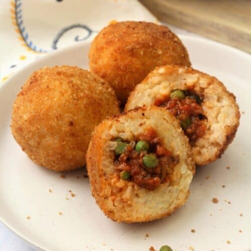 Sicilian arancini with ragu and peas cut open on plate with 2 whole arancini behind it.