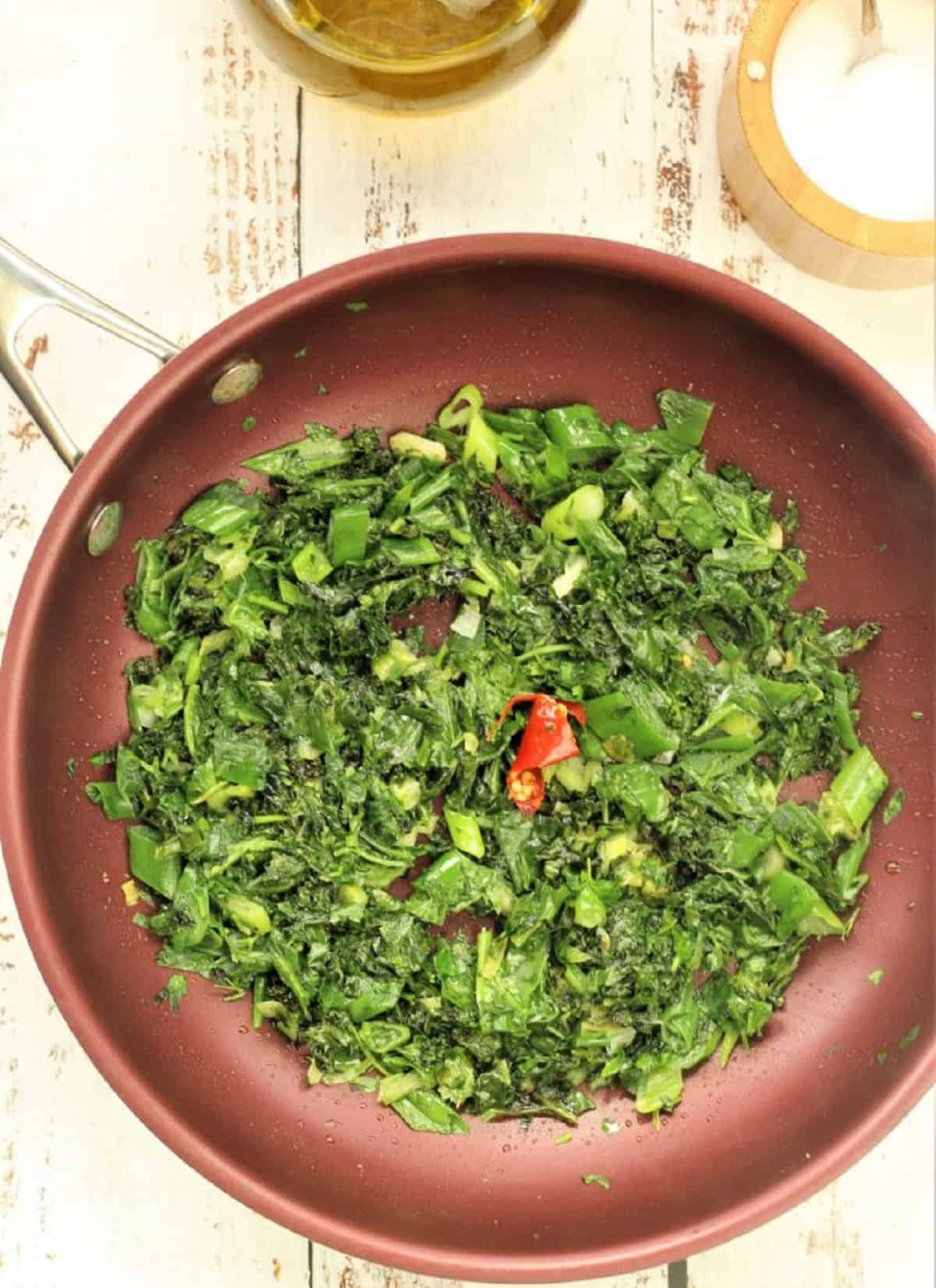 Fried greens with chili pepper in skillet.
