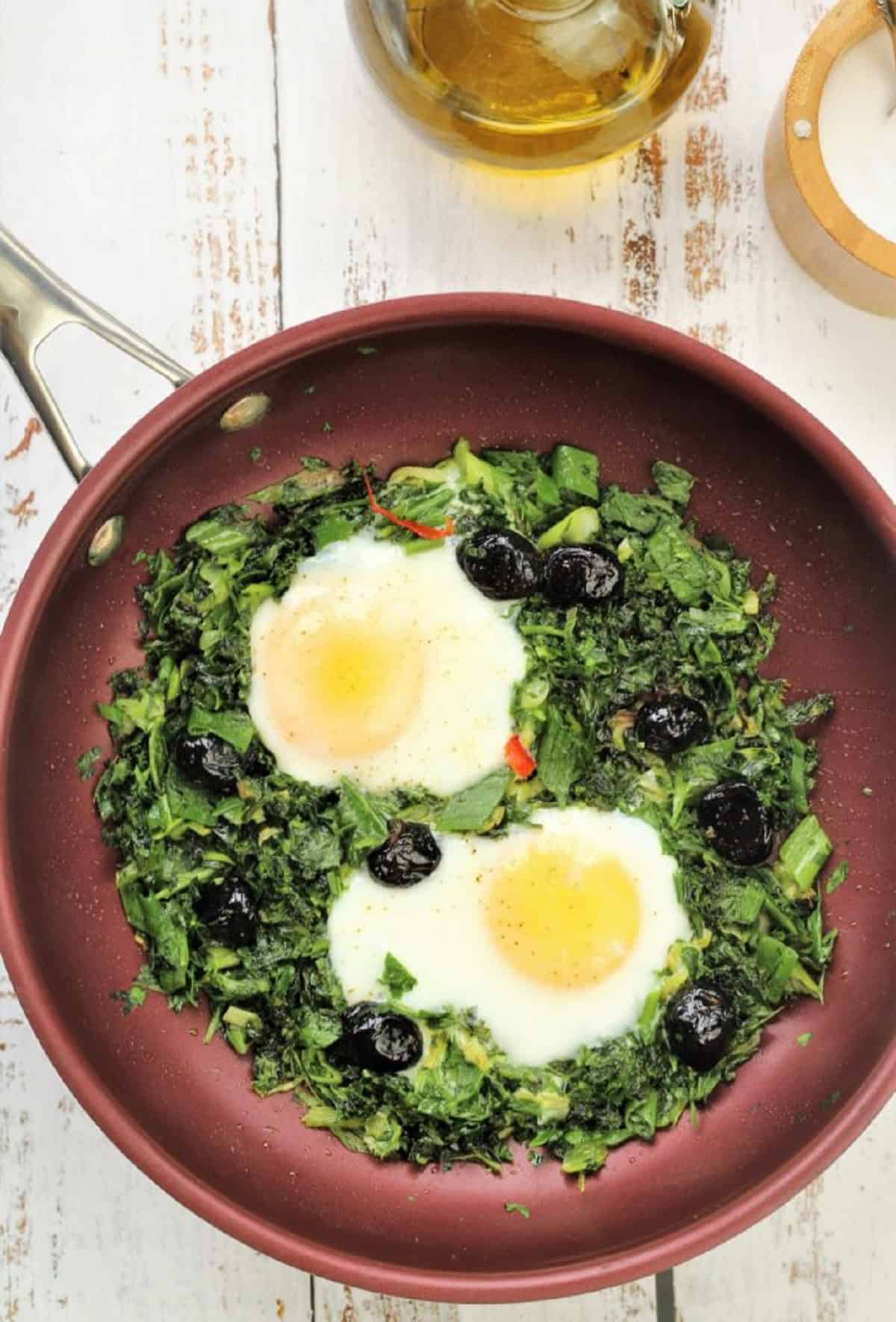 Fried eggs surrounded by greens in large skillet.