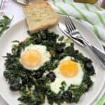 Fried eggs with greens plated along with sliced bread.