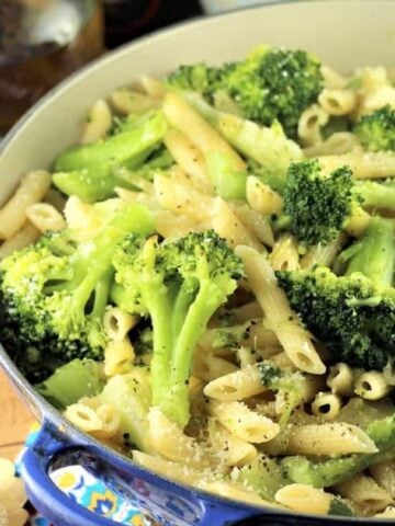 Broccoli pasta in large blue skillet topped with Parmigiano cheese.