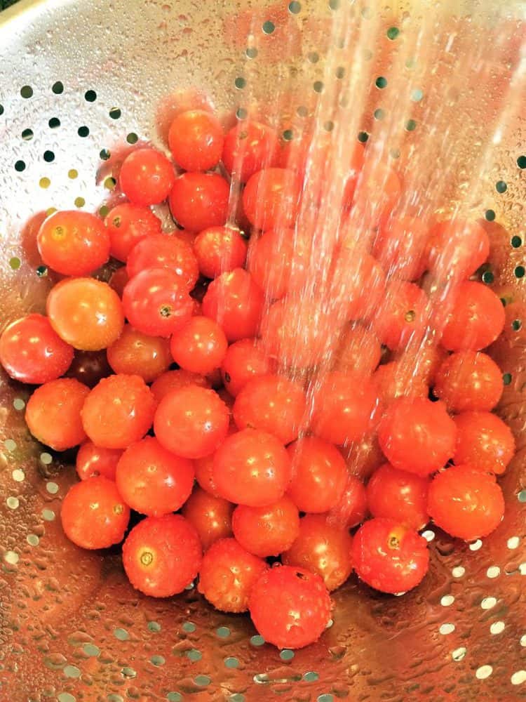 cherry tomatoes in a colander being rinsed