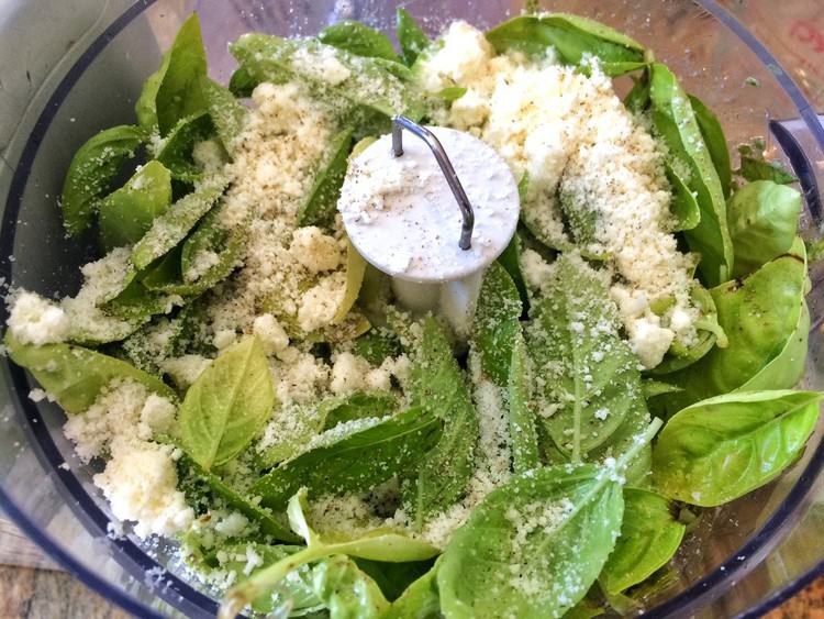food processor bowl filled with basil leaves and parmigiano
