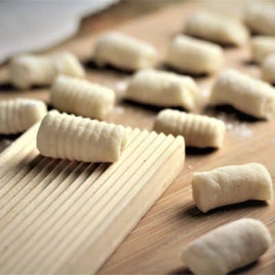 gnocchi board with a rolled gnocchi on it surrounded by other individual gnocchi