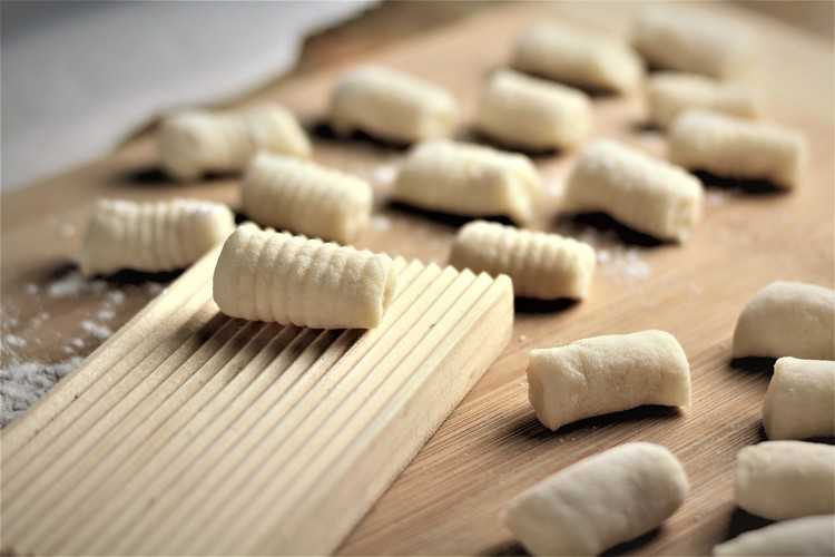gnocchi board with a rolled gnocchi on it surrounded by other individual gnocchi