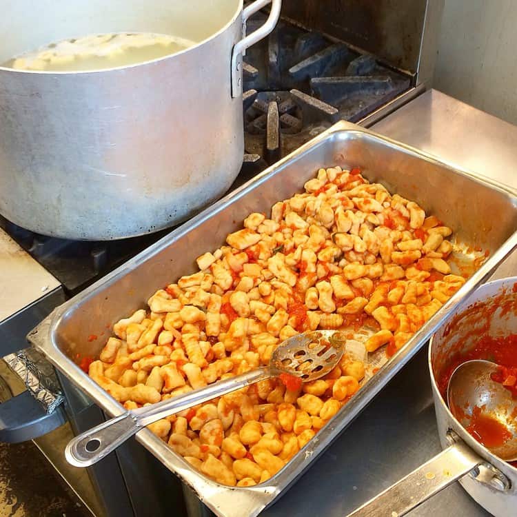 large pot of boiling water next a pan filled with cooked gnocchi in tomato sauce