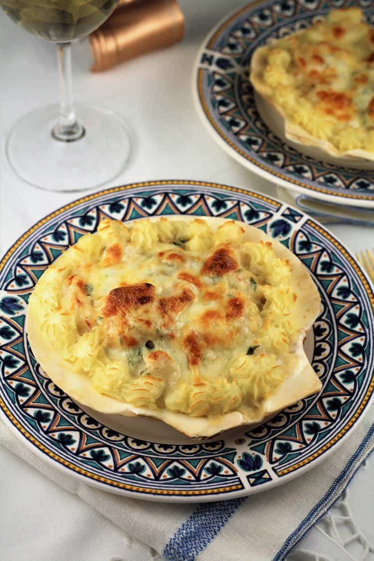 coquilles st-jacques served on a blue dish with wine glass behind it