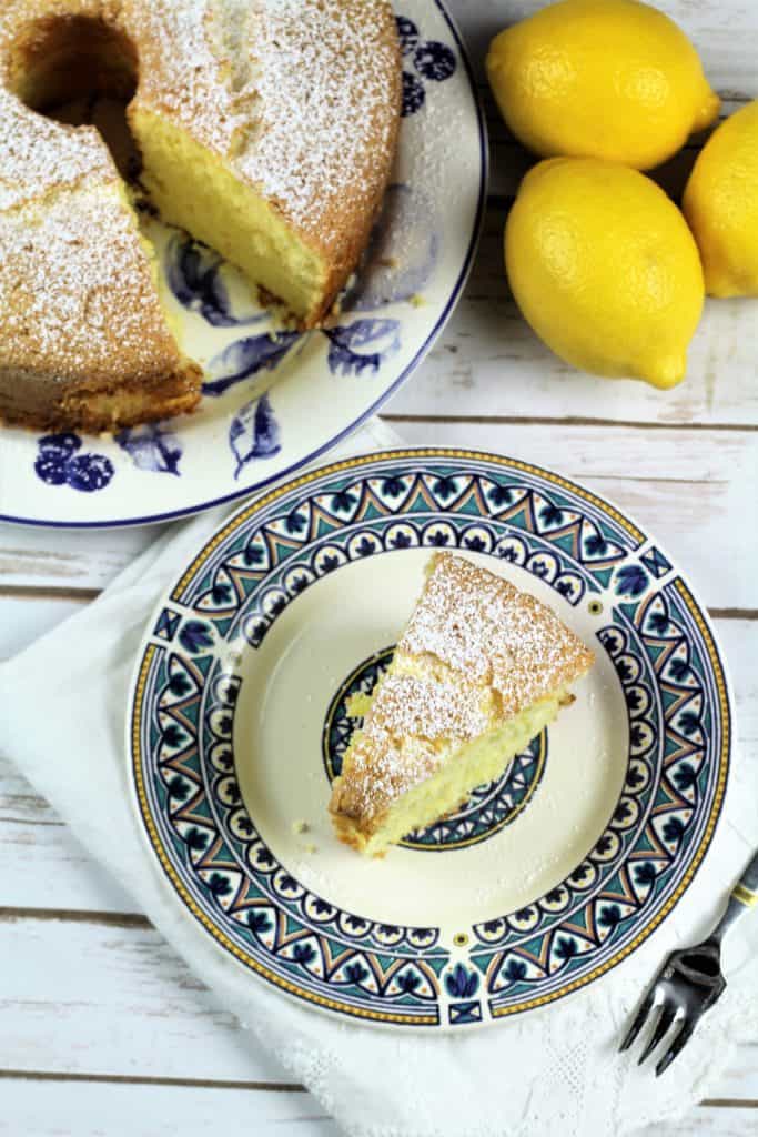 overhead view of slice of Nonna's Sponge Cake with full cake behind it and lemons on the side
