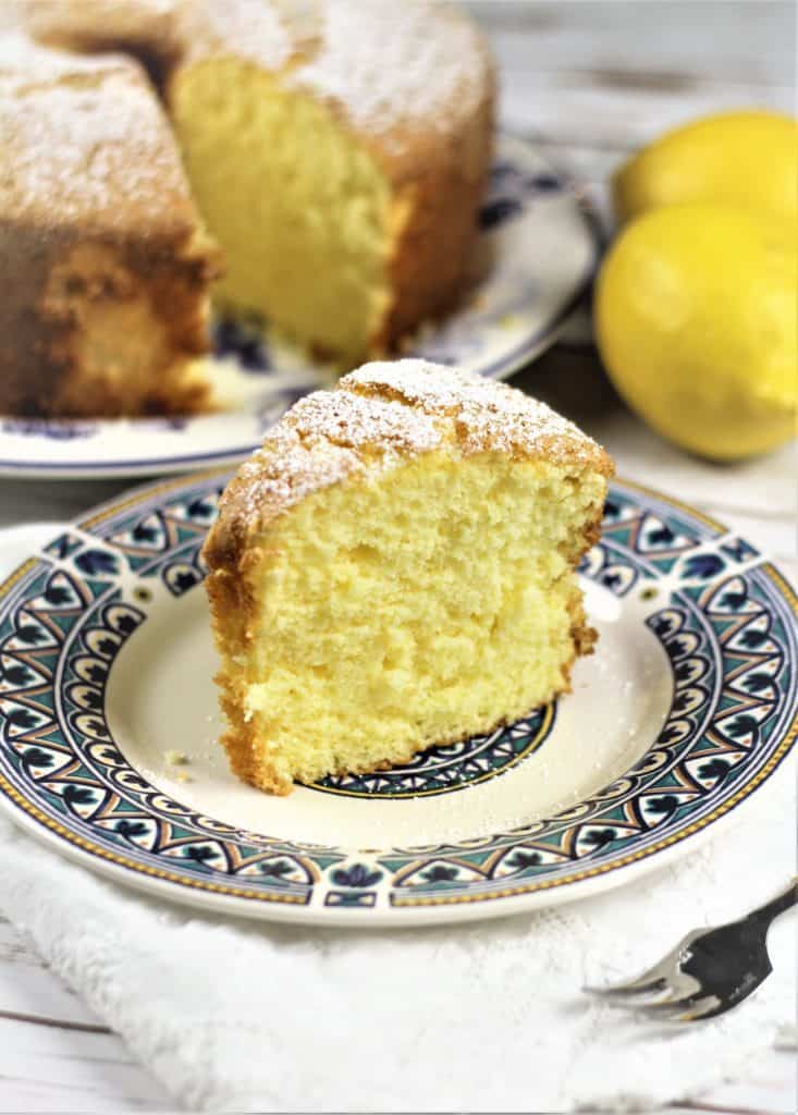 slice of Nonna's Sponge Cake with full cake in background and lemon on the side