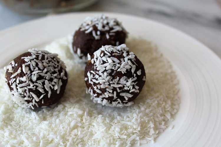 coconut covered date and nut truffles being rolled in coconut flakes