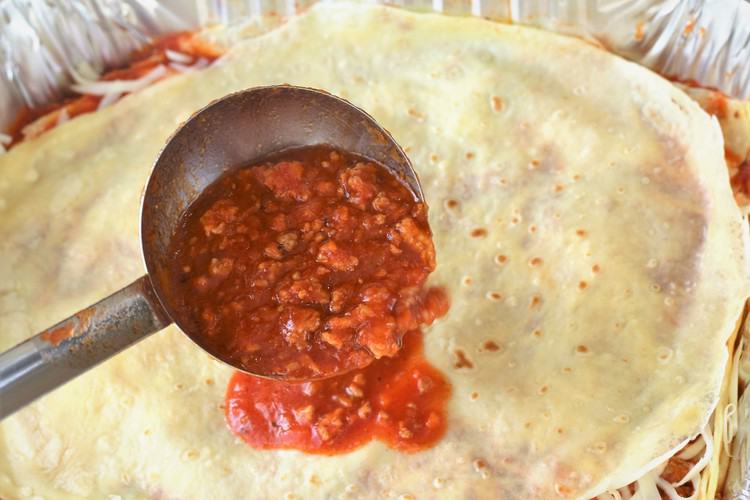 scooping meat sauce on a crepe in lasagna pan