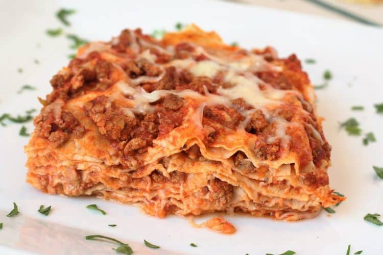  lasagna on a white plate sprinkled with parsley 