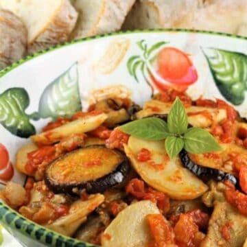 Baked eggplant with potatoes in tomato sauce in bowl topped with fresh basil.