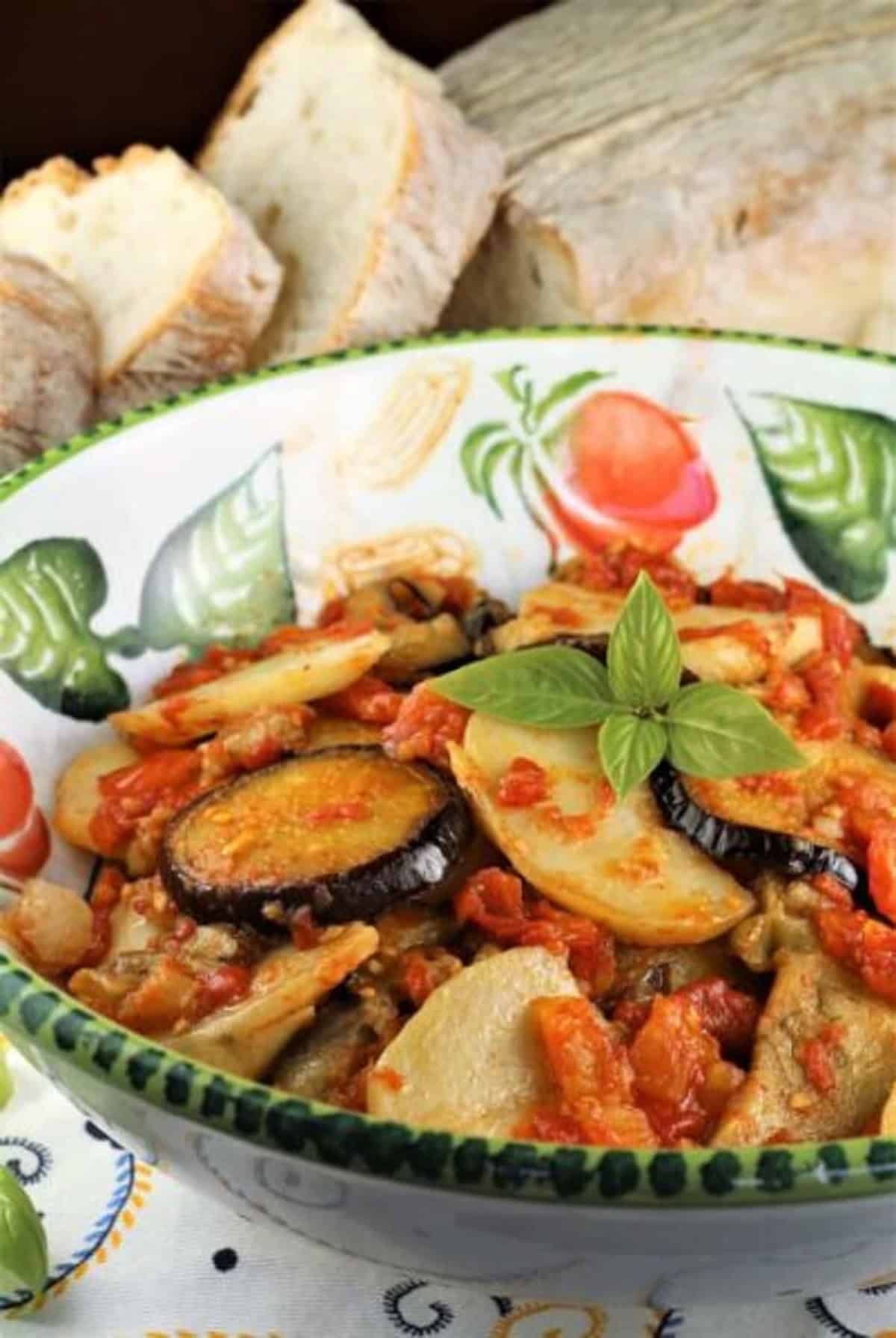 Baked Eggplant and Potatoes with Tomato Sauce Baked eggplant with potatoes in tomato sauce in bowl topped with fresh basil.