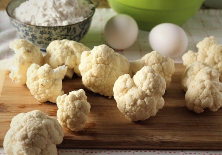 cauliflower florets on cutting board with eggs and flour in background