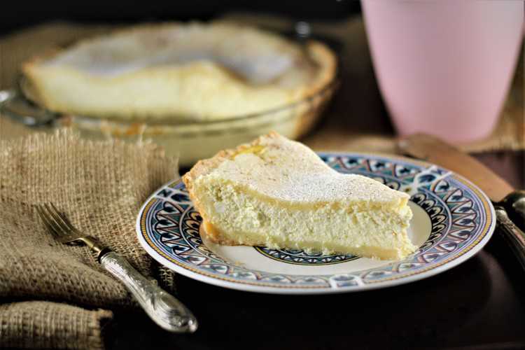 slice of sicilian ricotta pie on blue and white plate with pie plate behind it