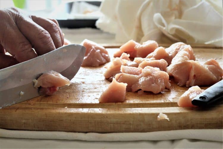 chopping chicken flesh into cubes with knife on wood board