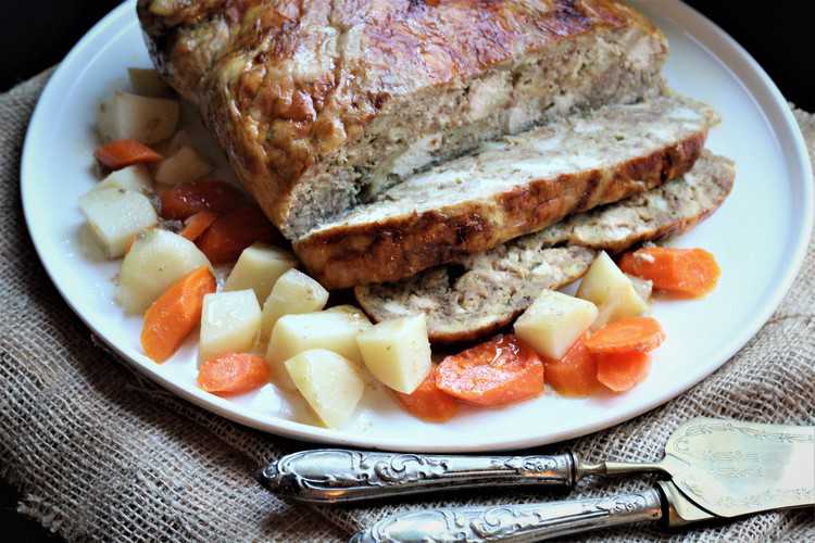 sliced stuffed chicken on white round platter with carrots and potatoes 