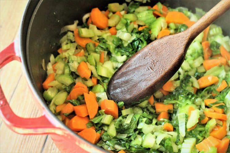 sauteing vegetables in a red pot with wooden spoon