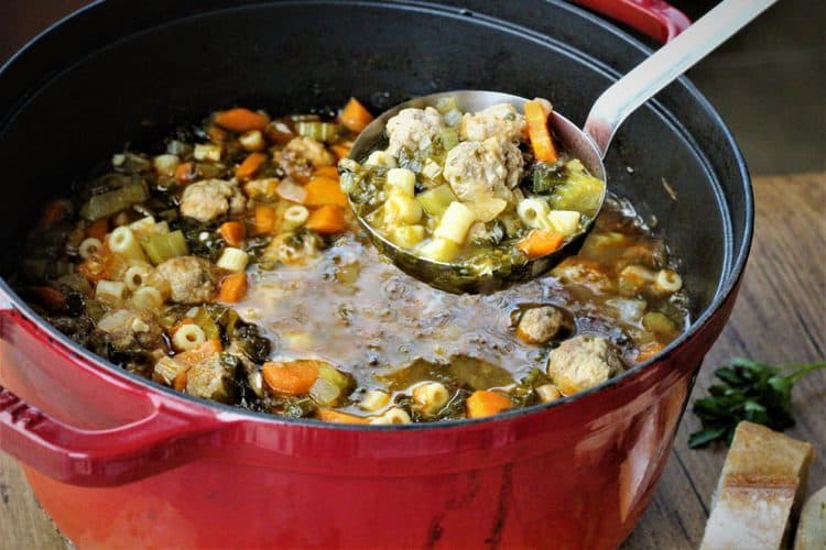 red soup pot with vegetable and meatball soup being ladled