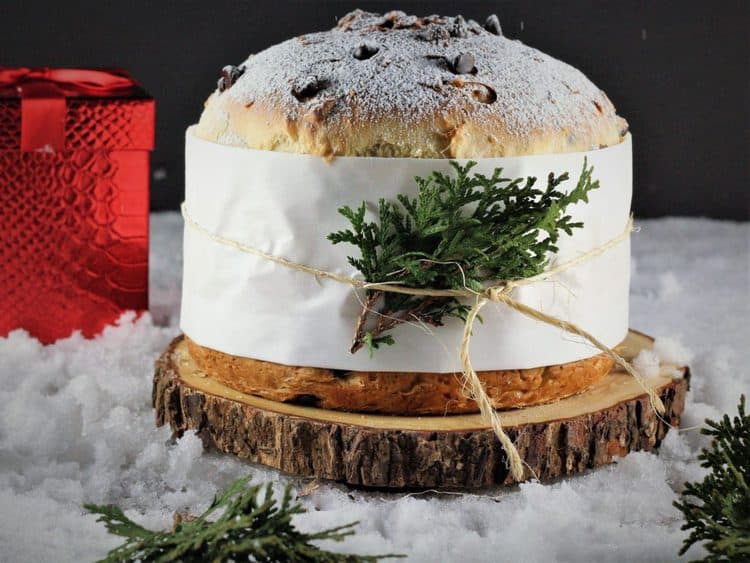 Panettone resting on a wood board surrounded by snow and pine branches
