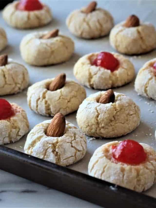 amaretti cookies topped with maraschinio cherries or almonds on baking sheet
