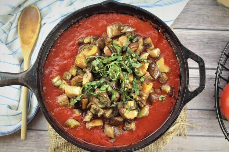 skillet with tomato sauce, eggplant pieces topped with chopped basil 