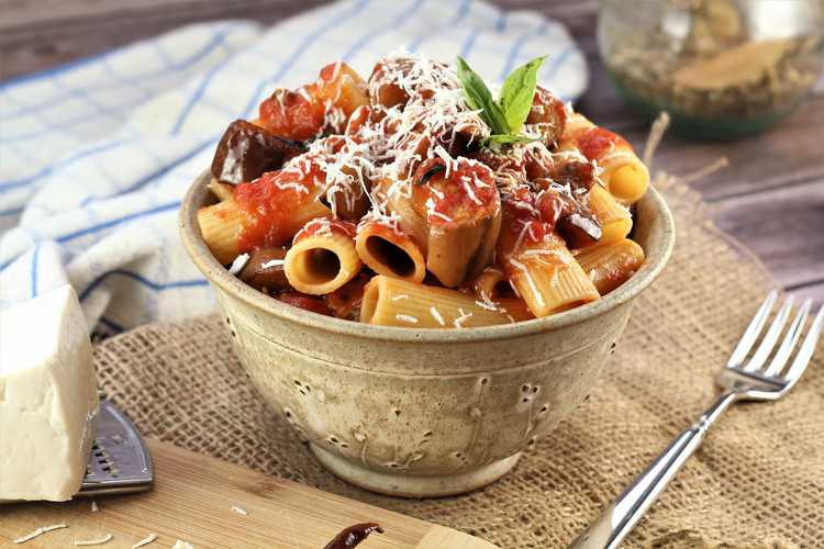 ceramic bowl filled with eggplant and pasta in sauce and fork on side
