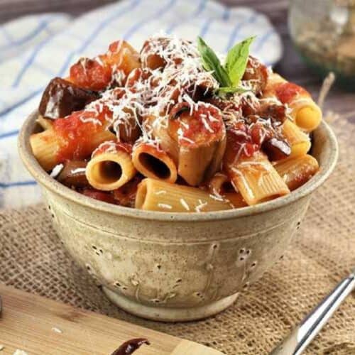 Pasta with eggplant in bowl topped with grated ricotta salata.