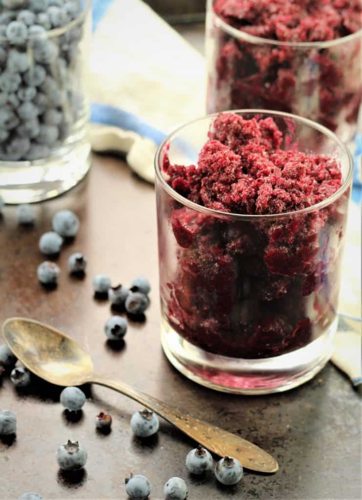 glasses filled with blueberry granita with spoon and fresh blueberries around it