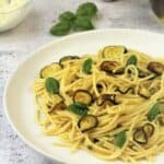 Spaghetti with fried zucchini on plate topped with basil leaves.