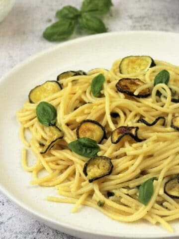 Spaghetti with oven fried zucchini in plate topped with basil.