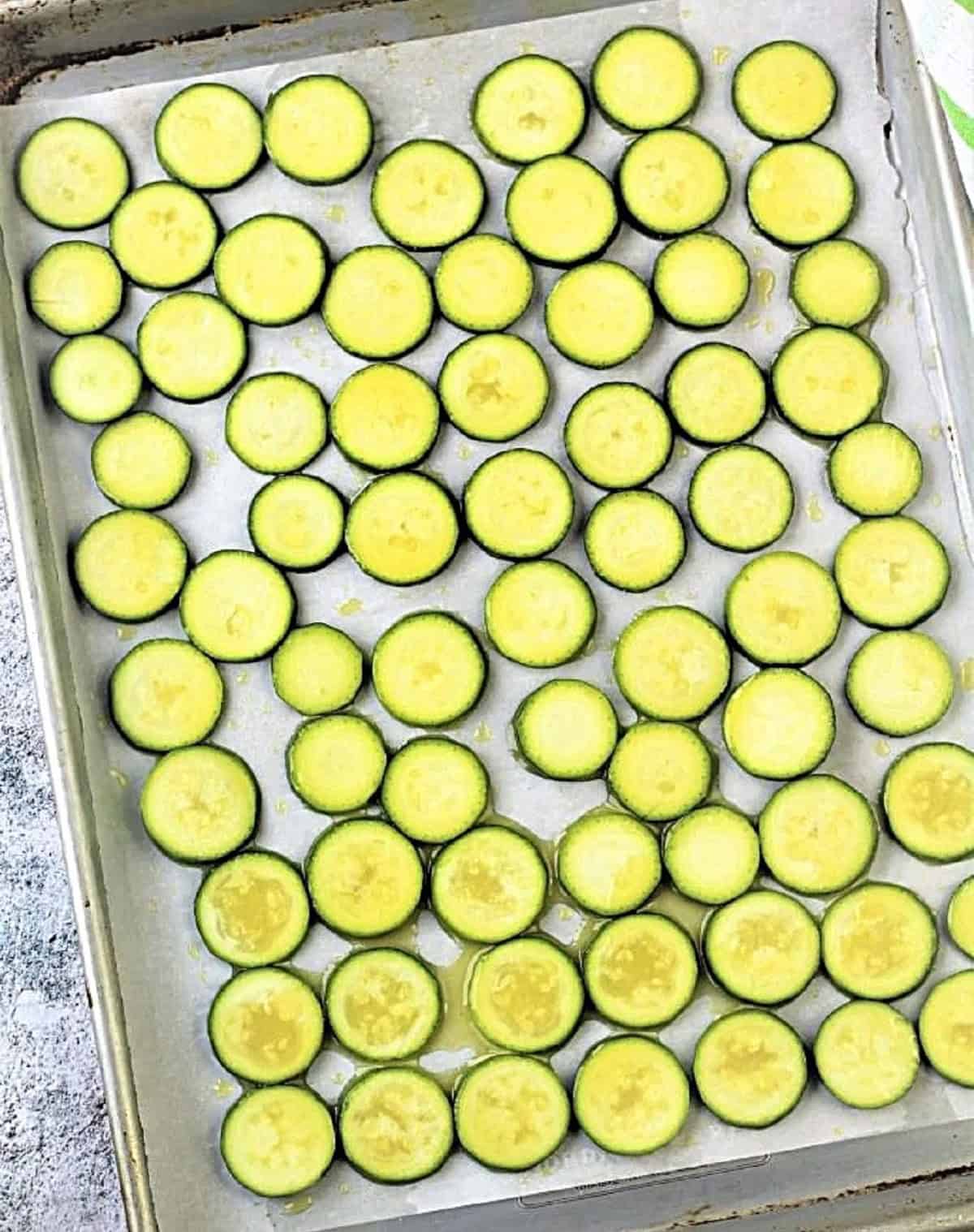 Sliced zucchini rounds coated in olive oil lined on baking sheet.