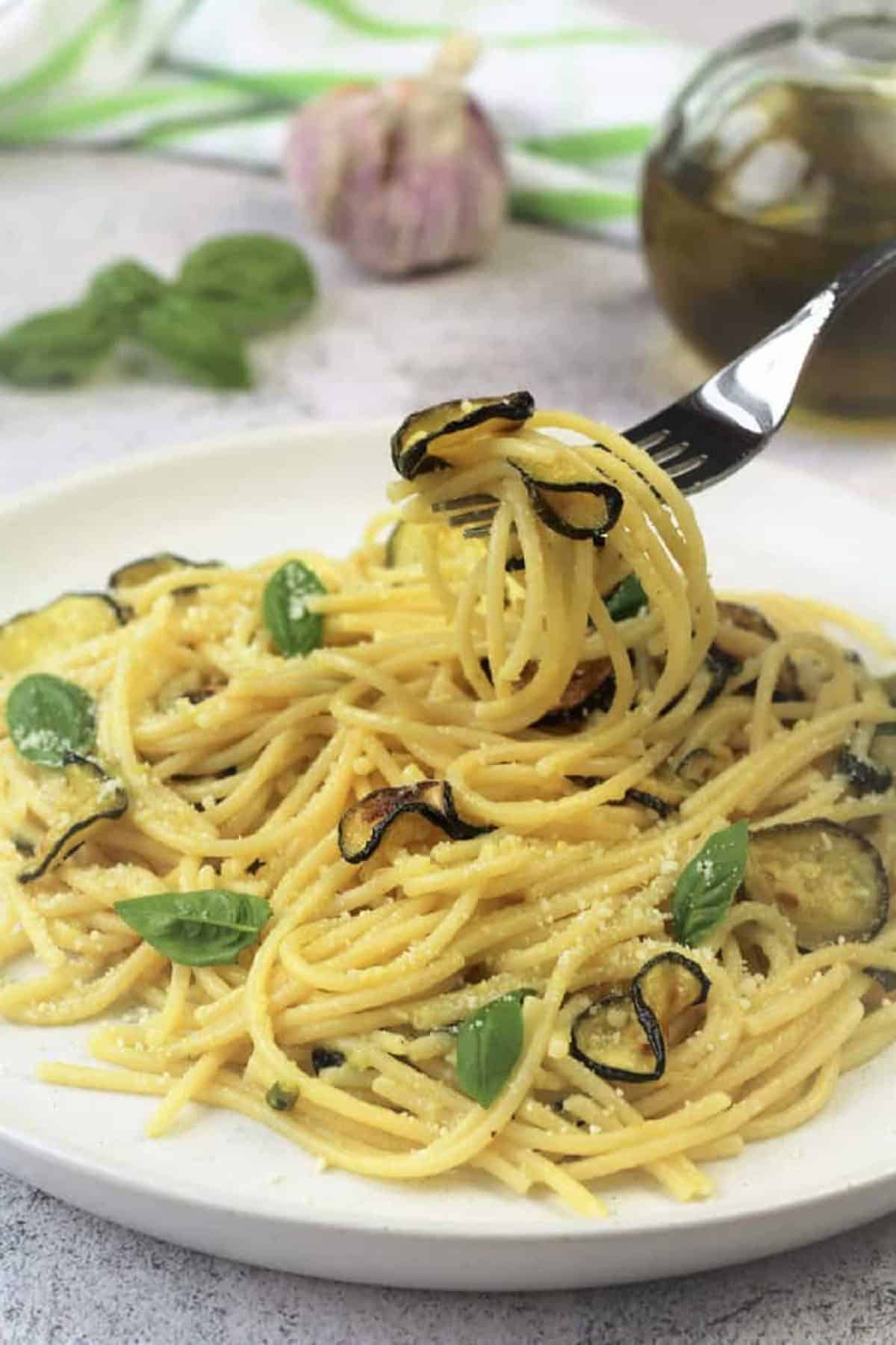 Spaghetti with zucchini twirled around fork in round plate.