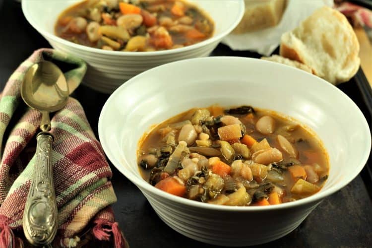 bowls of swiss chard and white bean stew with spoon on side and bread in background