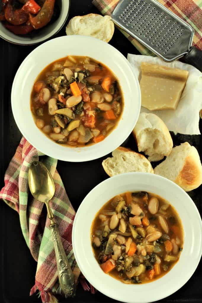 2 bowls of vegetable stew with bread, cheese and grater on side 