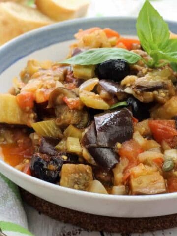 Sicilian eggplant caponata topped with fresh basil in bowl.
