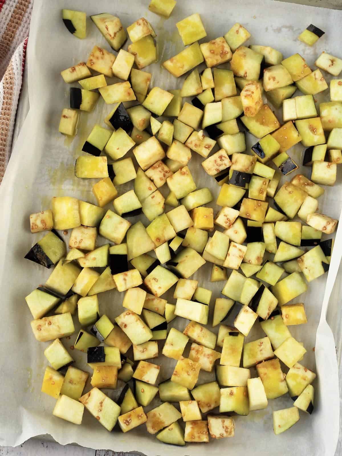Cubed eggplant tossed with olive oil on baking sheet for caponata recipe.