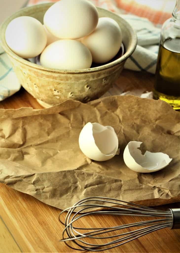 bowl of eggs with cracked egg shell and whisk in foreground