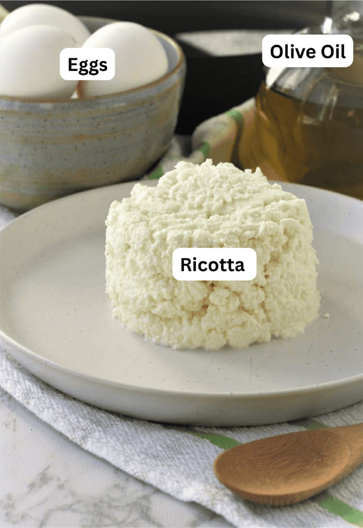 Ricotta mounded on a plate, a bowl of eggs and olive oil bottle.