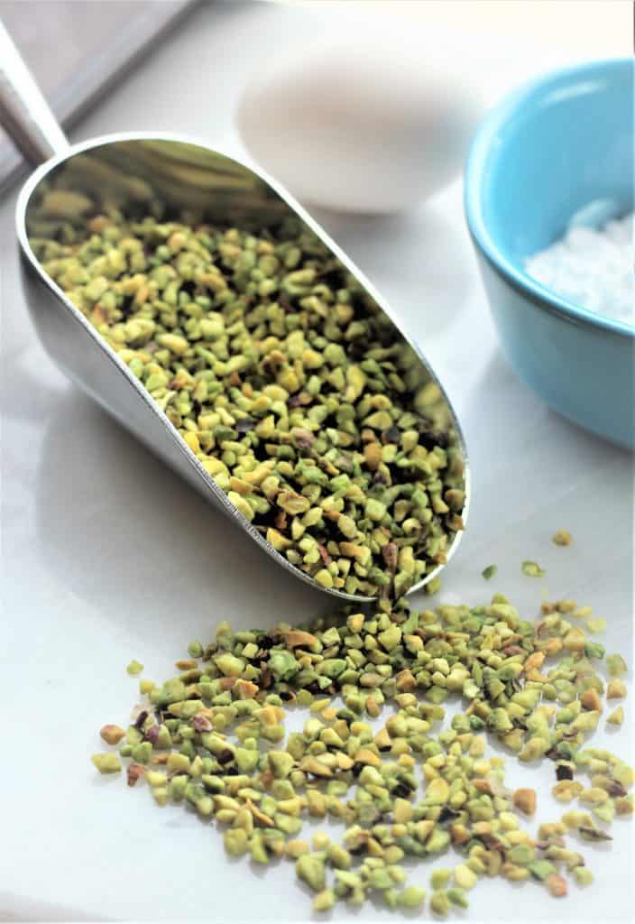 scoop of chopped pistachios overflowing on marble board with egg and blue bowl in background