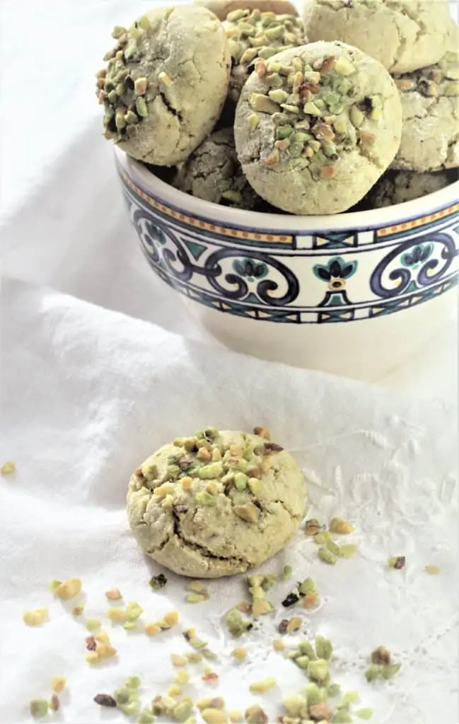 coffee cup filled with pistachio amaretti cookies with one cookie resting on the table cloth next to it