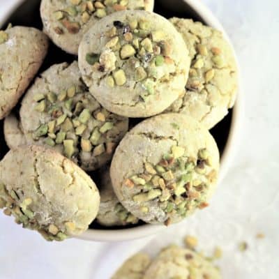overhead view of cup full of pistachio amaretti with one off to the side on the tablecloth