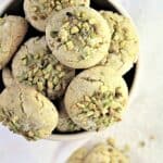 Pistachio amaretti in bowl with one cookie crumbled on the side.