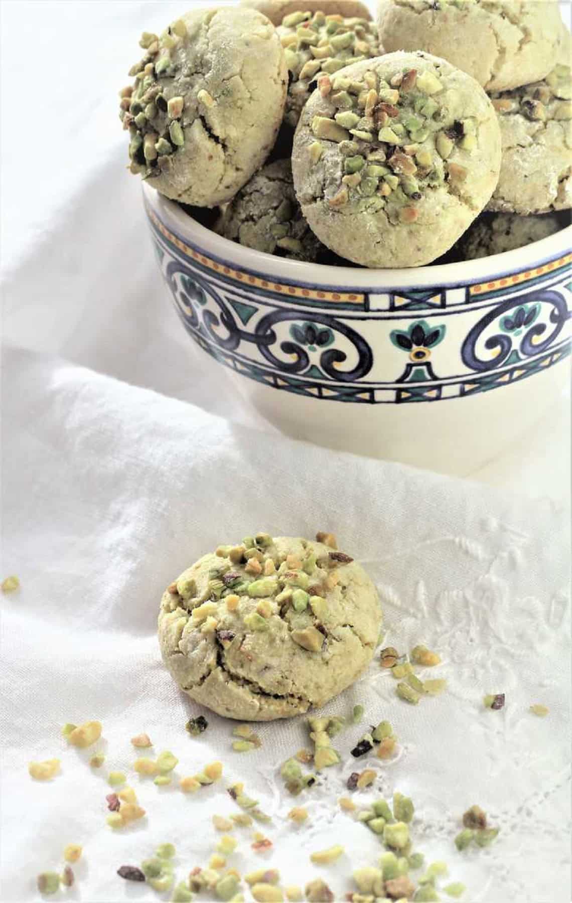 Pistachio amaretti cookies in cup with one cookie on the side.