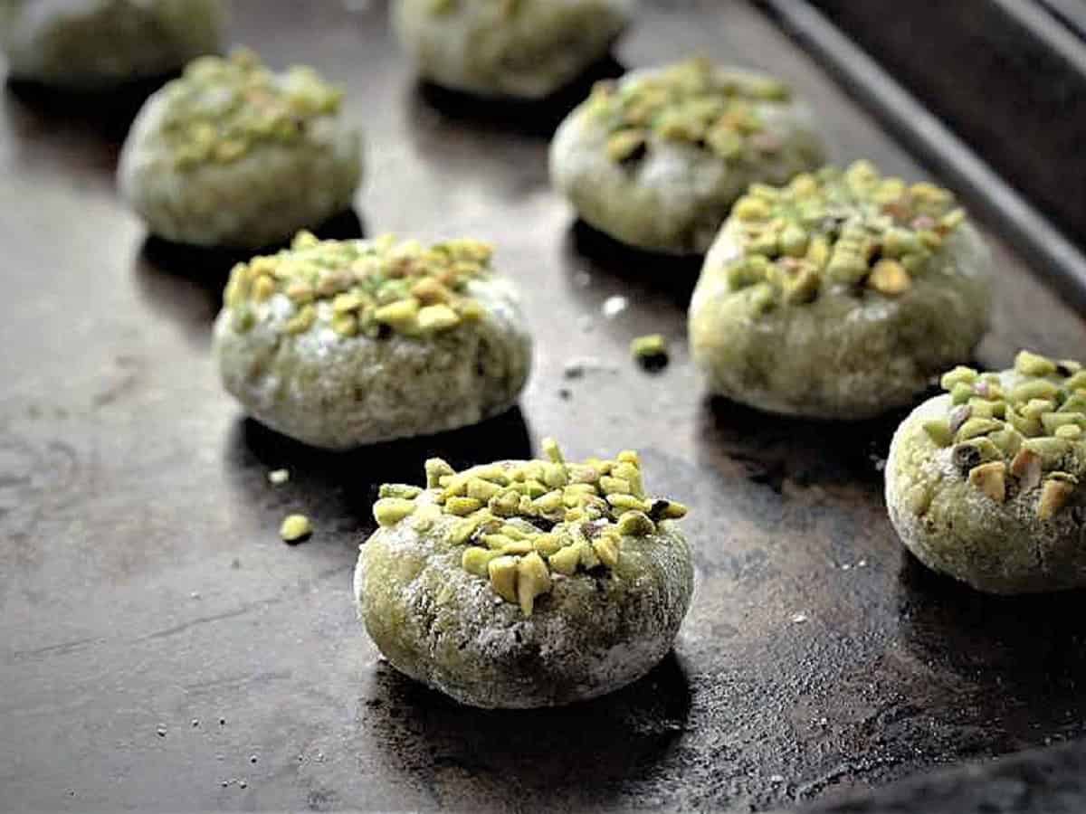 Pistachio amaretti topped with crushed pistachios on baking sheet.
