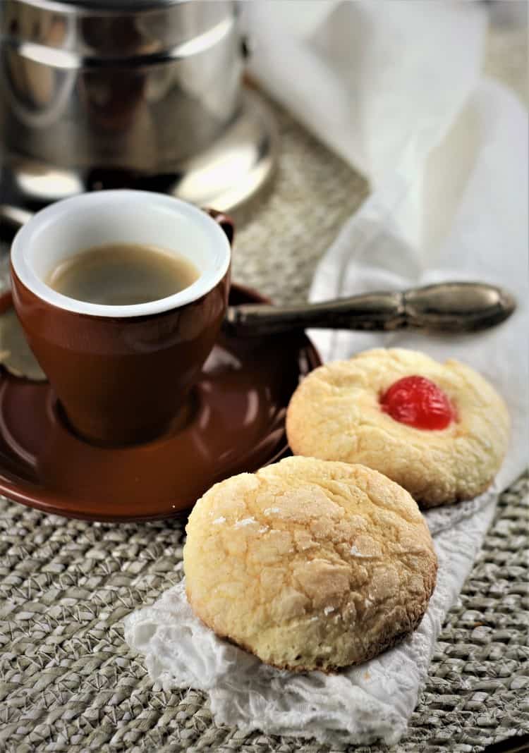 two cookies next to a cup of espresso with coffee maker in background