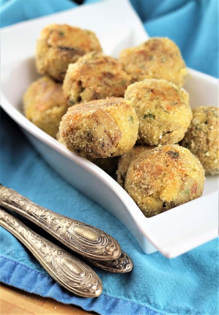 Eggplant meatballs piled on white plate with utensils on side.