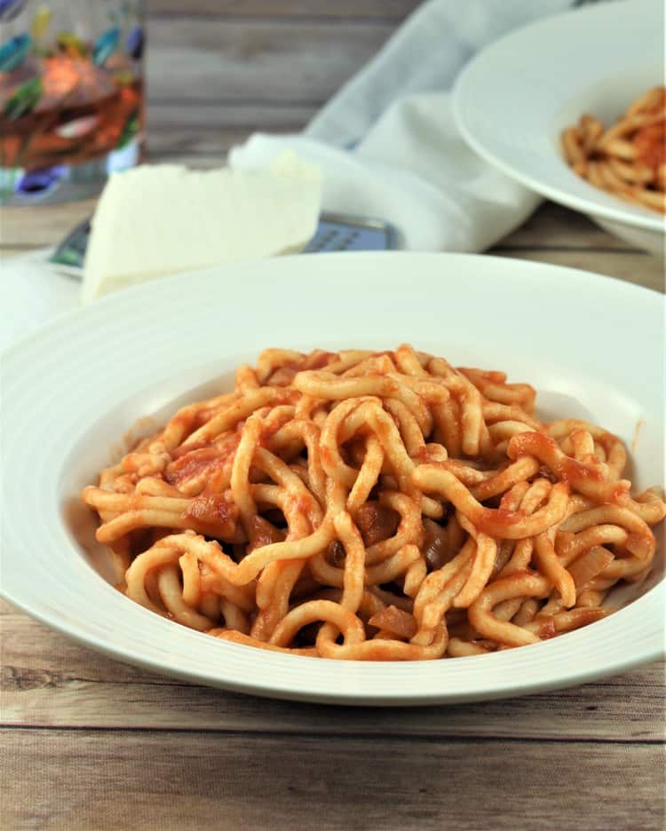 plate filled with maccaruna in tomato sauce with wedge of cheese and glass in background